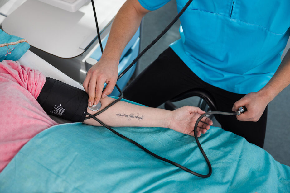 Potilaan ja hoitajan kädet näkyvissä, mitataan verenpainetta.