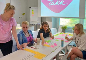 Neljä henkilöä kokoontunut valkoisen pöydän ympärille, pöydällä muistilappuja