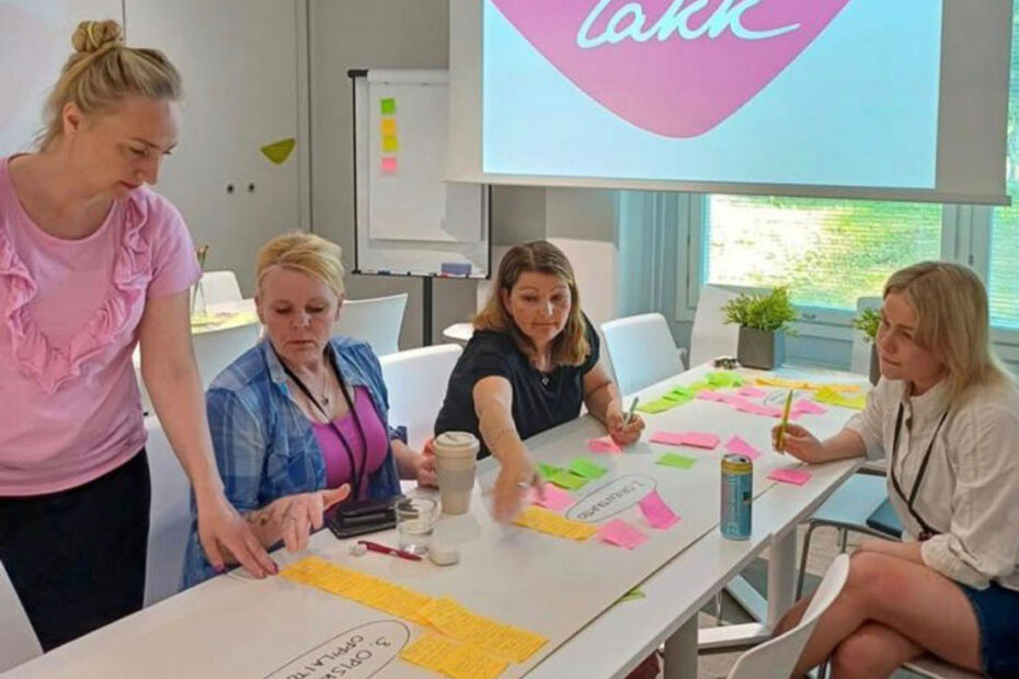 Neljä henkilöä kokoontunut valkoisen pöydän ympärille, pöydällä muistilappuja