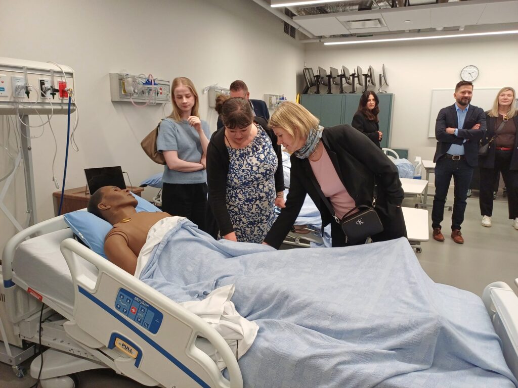 Ihmisiä kumartuneena nuken ylle sote-alan hoitoluokassa.